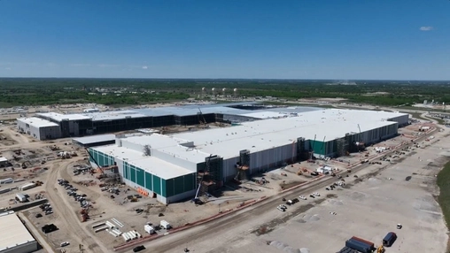 Aerial view of a gigafactory under construction on a flat industrial site with open land and blue sky