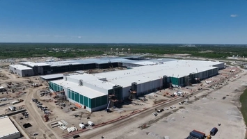 Aerial view of a gigafactory under construction on a flat industrial site with open land and blue sky