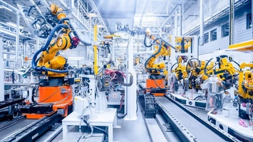Multiple yellow robotic arms working along an automated production line inside a well-lit gigafactory floor